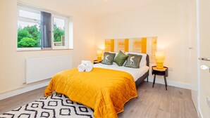 A bedroom with a bed, a window, a radiator, a bedside table with a lamp, and a rug. - Spacious 2BR Flat Summertown Sleeps 7 5 Star (Oxford)