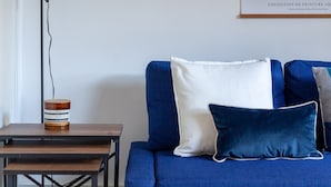 A room with a blue sofa, a small table with a lamp, and artwork on the walls. - 3 Bed House With Garden in London Fields (London)