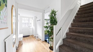A staircase leading to a landing with a potted plant, a white bench, and a door with frosted glass panels. - 3 Bed House With Garden in London Fields (London)