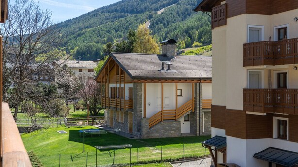 Un edificio in stile chalet con facciata in pietra, balcone in legno e una scala che conduce a un patio in legno.