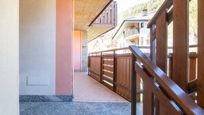 Un corridoio con ringhiera in legno, parete in pietra e vista su edifici sullo sfondo.