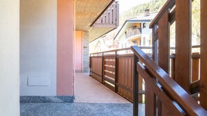 A corridor with a wooden railing, a stone wall, and a view of buildings in the background. - Palú Elf Den in the heart of Aprica (Aprica)