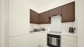 Cozinha compacta com armários brancos, forno preto, pia de aço inoxidável e backsplash de mármore.
