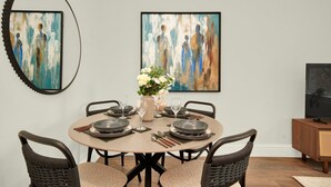 Uma sala de jantar com uma mesa redonda, seis cadeiras e duas pinturas abstratas na parede.