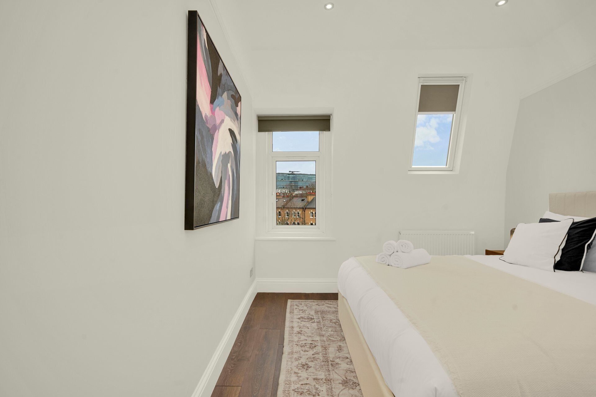 A bedroom with a bed, a window, a radiator, and a painting on the wall.