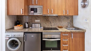 Cocina compacta con armarios de madera, microondas, tostadora, lavaplatos, fregadero y lavadora.