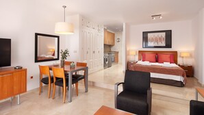 Habitación de hotel con cama, escritorio, silla, televisión, mesa de comedor y zona de cocina.