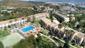 Un hotel con piscina, varias edificaciones y montañas al fondo.