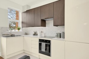 Eine moderne Küche mit weißen Schränken, einem eingebauten Backofen und einem Fenster mit Blick auf eine Backsteinmauer.