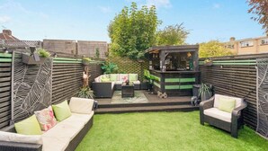 Een terras met een zithoek, een kleine bar en een groen gazon.