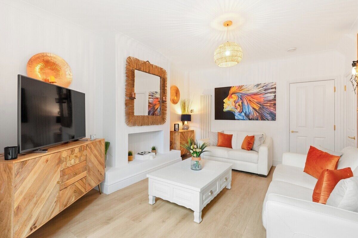 A modern living room with a TV, white sofas, a coffee table, and artwork on the walls.
