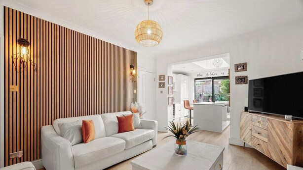 Een moderne woonkamer met een witte bank, een salontafel, een tv op een houten kast, en een keuken die zichtbaar is door een open doorgang.