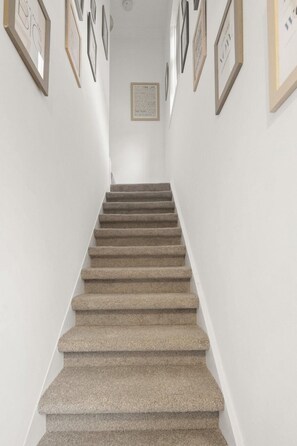Eine Treppe mit Teppichbelag, weißen Wänden und gerahmten Kunstwerken an den Seiten.