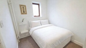 Ein Schlafzimmer mit einem Bett, einem Fenster, einem Bild an der Wand und einem kleinen Regal.