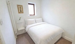 Ein Schlafzimmer mit einem Bett, einem Fenster, einem Bild an der Wand und einem kleinen Regal.