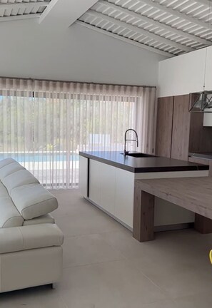 A modern kitchen with a built-in island, a dining area with a bench, and a view of a swimming pool through large windows. - 4-bedroom villa with private pool in Armação de Pêra (Armação de Pêra)