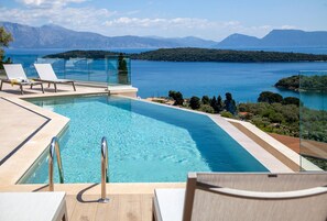 A swimming pool with clear water, lounge chairs, and a view of a lake and mountains. - Smirties Villa Phaena 2bed (Lefkada)
