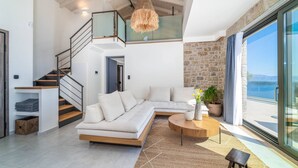 A modern living room with a sofa, a coffee table, a staircase, and a view of the sea. - Smirties Villa Phaena 2bed (Lefkada)