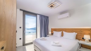 A hotel room with a large bed, a wooden headboard, a view of the sea, and a sliding glass door. - Smirties Villa Phaena 2bed (Lefkada)