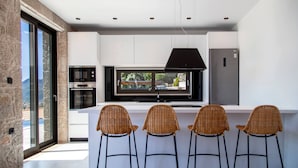 A modern kitchen with a large island, built-in appliances, and a view through the window. - Smirties Villa Phaena 2bed (Lefkada)
