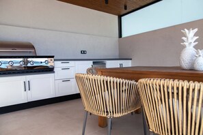Une cuisine moderne avec des armoires blanches, un plan de travail en bois et un barbecue. On y trouve des chaises en osier et une table à manger.
