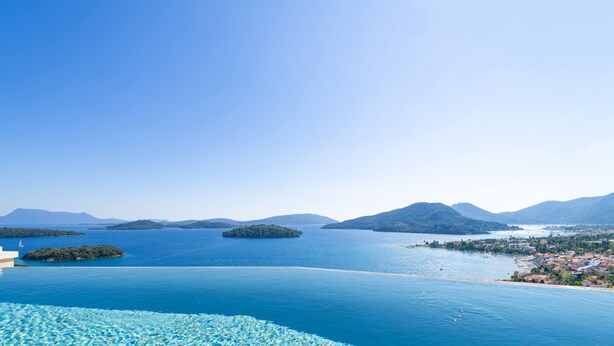 A clear view of a large swimming pool with a glass edge, surrounded by a coastal landscape with mountains and a small island. - Smirties Villa Phaena 2bed (Lefkada)