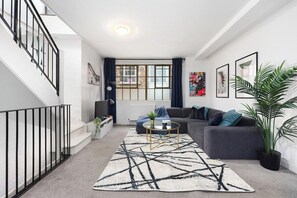 Ein modernes Wohnzimmer mit Treppe, einem grauen Sofa, einem Couchtisch und einem großen Fenster mit Vorhängen.