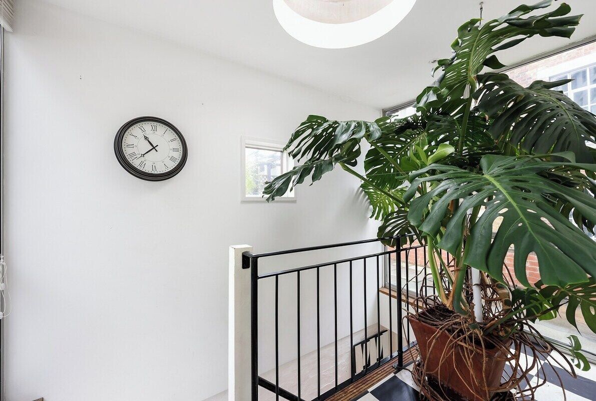 A staircase with a potted monstera plant, a wall clock, and a window.