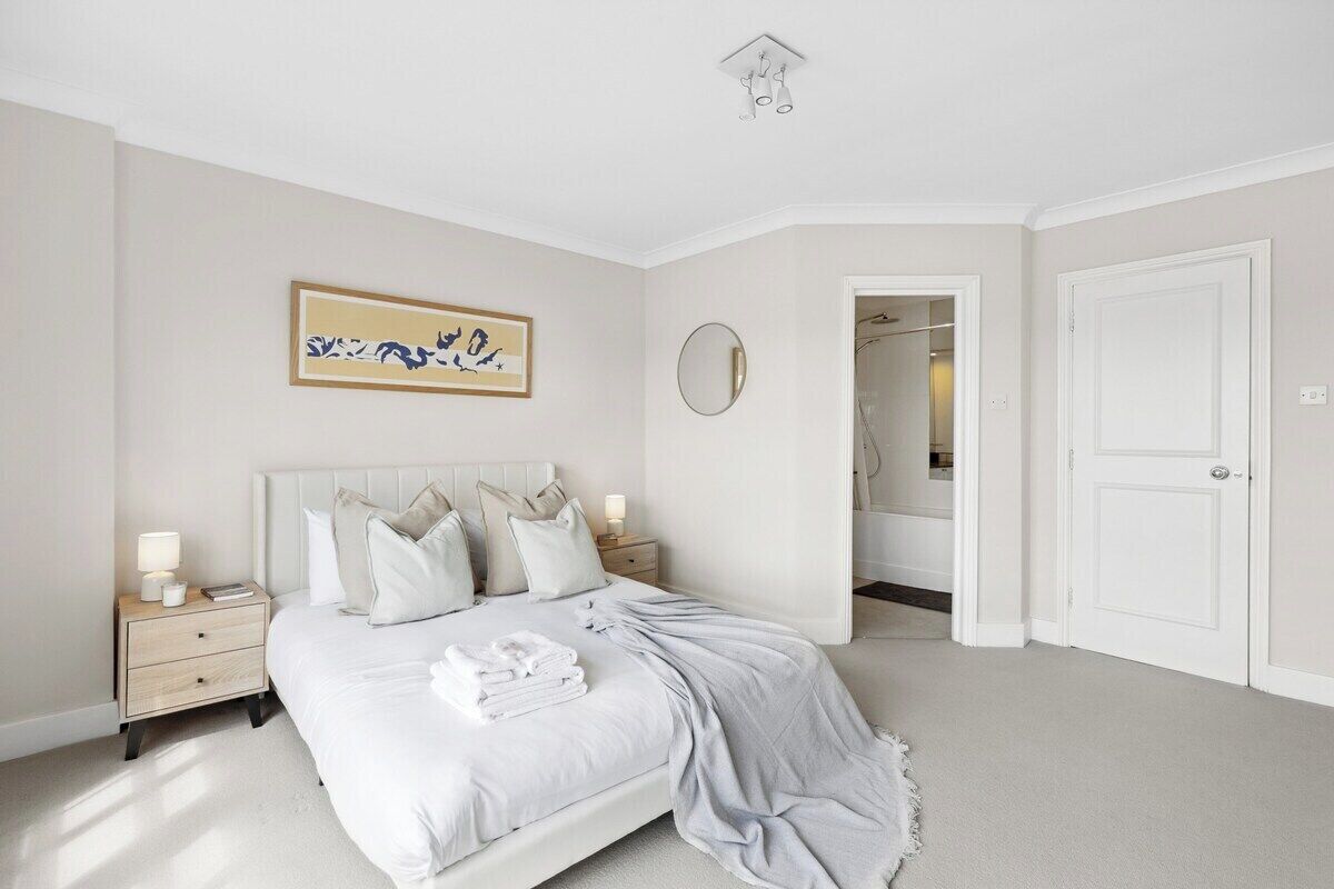 A bedroom with a bed, bedside tables, a nightstand, a mirror, and a door leading to another room.
