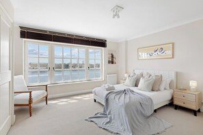 Ein Schlafzimmer mit großem Fenster, einem Bett, einem Sessel, einem Nachttisch und einer Heizung.