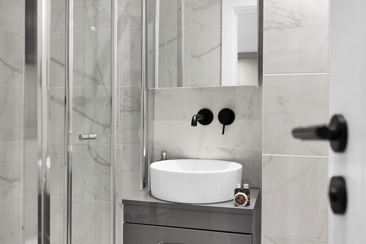 A modern bathroom with a glass shower enclosure, a white sink, and a mirror above it.