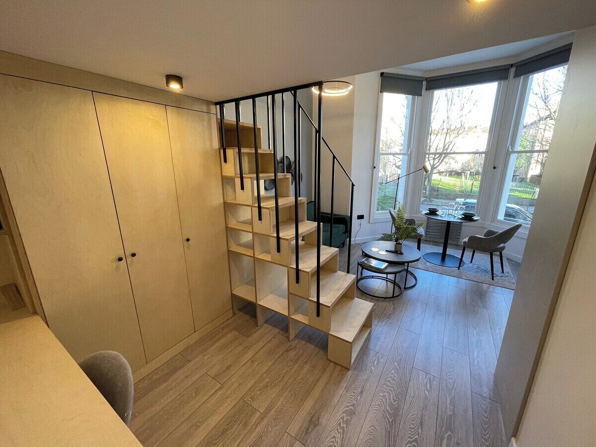 Et moderne interiør med en trætrappe, et spiseområde og udsigt gennem store vinduer.