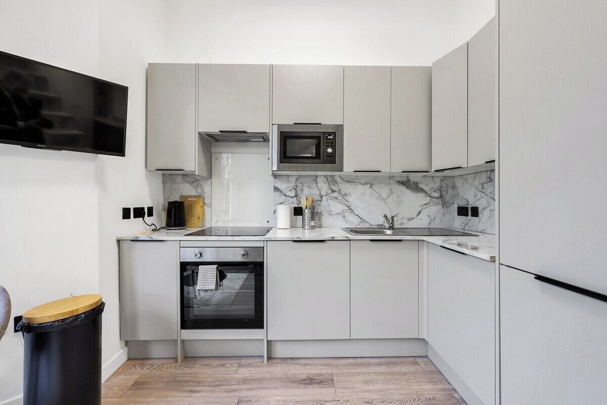 Une cuisine moderne avec des armoires blanches, un four à micro-ondes encastré, une cuisinière et une poubelle noire.