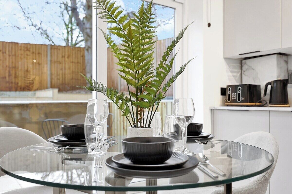 A modern dining area with a glass table, black plates, and clear glasses.
