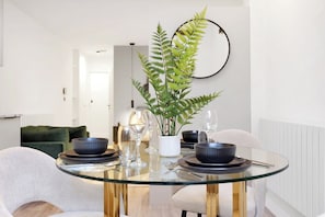 A dining table with a glass top, surrounded by chairs, with a fern plant in the center. - Sleek & Stylish Studio in London (London)