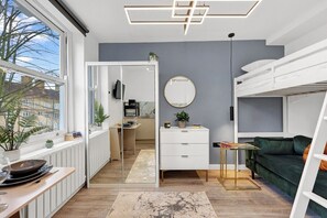 Un intérieur moderne comprenant une cuisine, un coin repas et un espace de vie, avec notamment un lit superposé, un miroir rond et une vue à travers une porte vitrée.