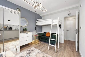 A room with a bunk bed, a desk with a mirror, a dresser, a small side table, and a green sofa. - Single Studio Flat close to Camden! (London)