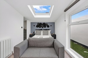A modern bedroom with a skylight, a bed with patterned pillows, a grey sofa, and a large window. - Large Studio Flat in London - With Terrace! (London)