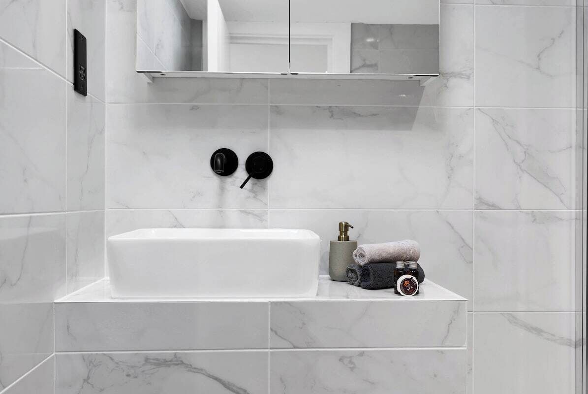A modern bathroom with a large rectangular bathtub, a towel dispenser, and a mirror above the sink.