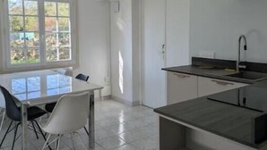 A modern kitchen with a dining area, large windows, and a view of the outdoors. - Bright 2-Bedroom Apartment in the Heart of the Vineyards – 25 Minutes from Bordeaux (Prignac-et-Marcamps)