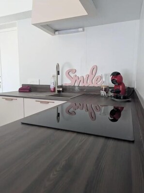 A modern kitchen with a dark countertop, a sink, a faucet, a pink 'Smile' sign, and a red helmet on the counter. - Bright T2 in the heart of the vineyards - 25 min from Bordeaux (Prignac-et-Marcamps)