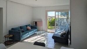 A modern living room with a blue sofa, a glass coffee table, and a ceiling fan. - Bright 2-Bedroom Apartment in the Heart of the Vineyards – 25 Minutes from Bordeaux (Prignac-et-Marcamps)