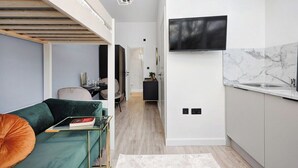 Eine moderne Wohnung mit Schlafzimmer im oberen Bereich, einer Küche mit Marmorfliesenspiegel und einem an der Wand befestigten Flachbildfernseher.