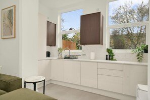 Eine moderne Küche mit weißen Schränken, einer Marmorarbeitsplatte und einem Fenster mit Blick auf Bäume.