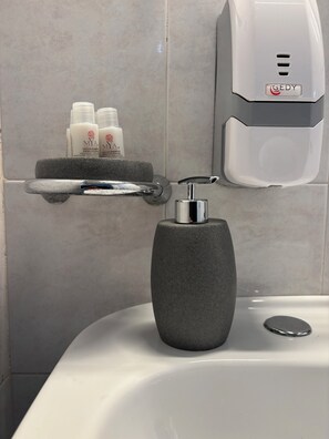 Ein Badezimmer mit einem modernen Waschbecken, einer Seifenspender und einem Ablagefach mit Pflegeprodukten.
