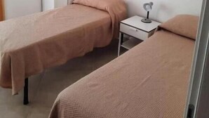 Una habitación con dos camas, un armario y una mesita de noche con lámpara.