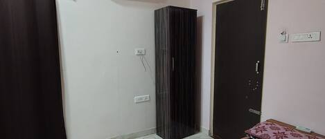 A bedroom with a bed, a ceiling fan, an air conditioning unit, a wardrobe, and a door.