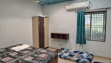 A bedroom with a bed, a wardrobe, a bedside table, a window with curtains, and an air conditioning unit.
