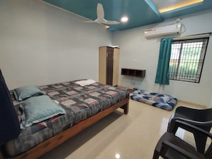 Ein Schlafzimmer mit Bett, Stuhl, Kleiderschrank, Regal und Klimaanlage.