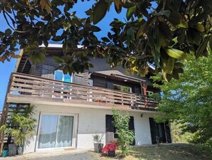 Un edificio a due piani con un balcone, una porta scorrevole in vetro e un piccolo giardino.